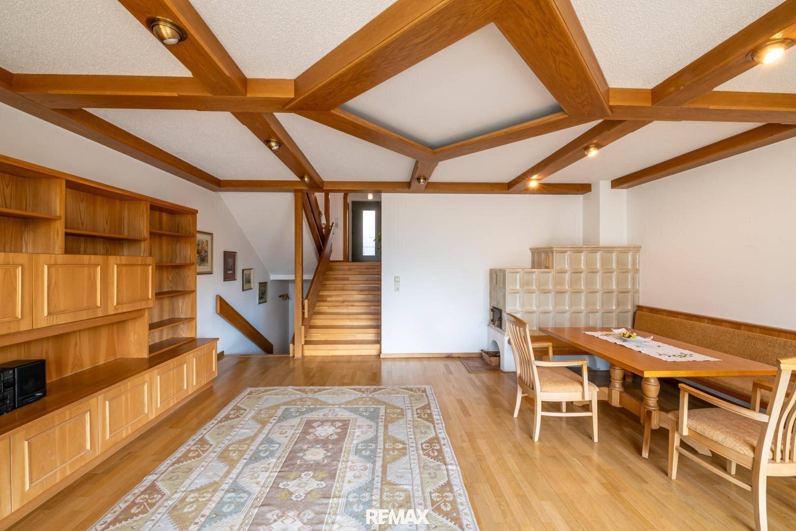 Heller Wohn- und Essbereich mit Holzbalkendecke, Parkettboden und traditionellem Kachelofen.