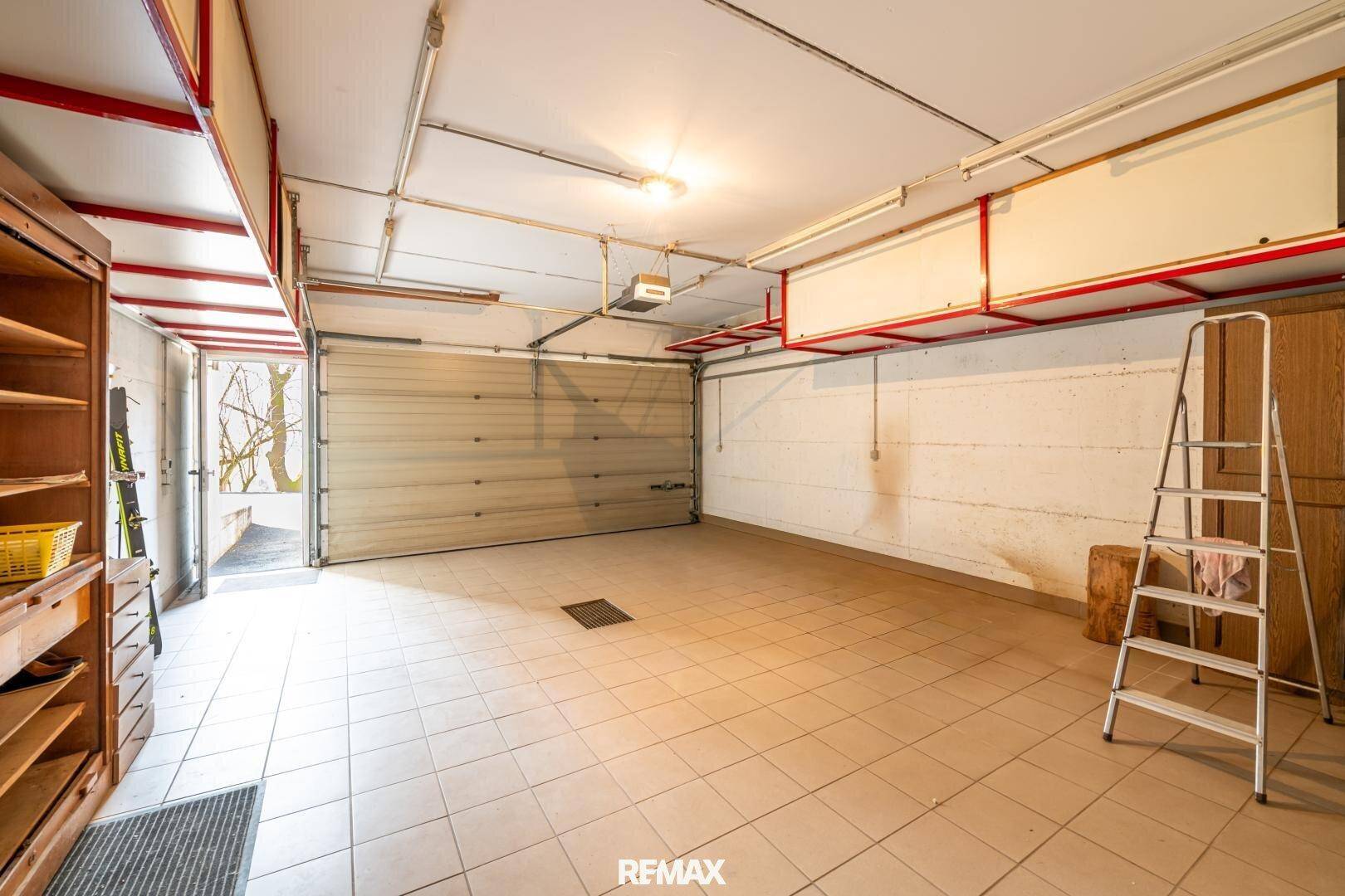 Geräumige Garage mit Fliesenboden, Rolltor und ausreichend Platz für Fahrzeuge.