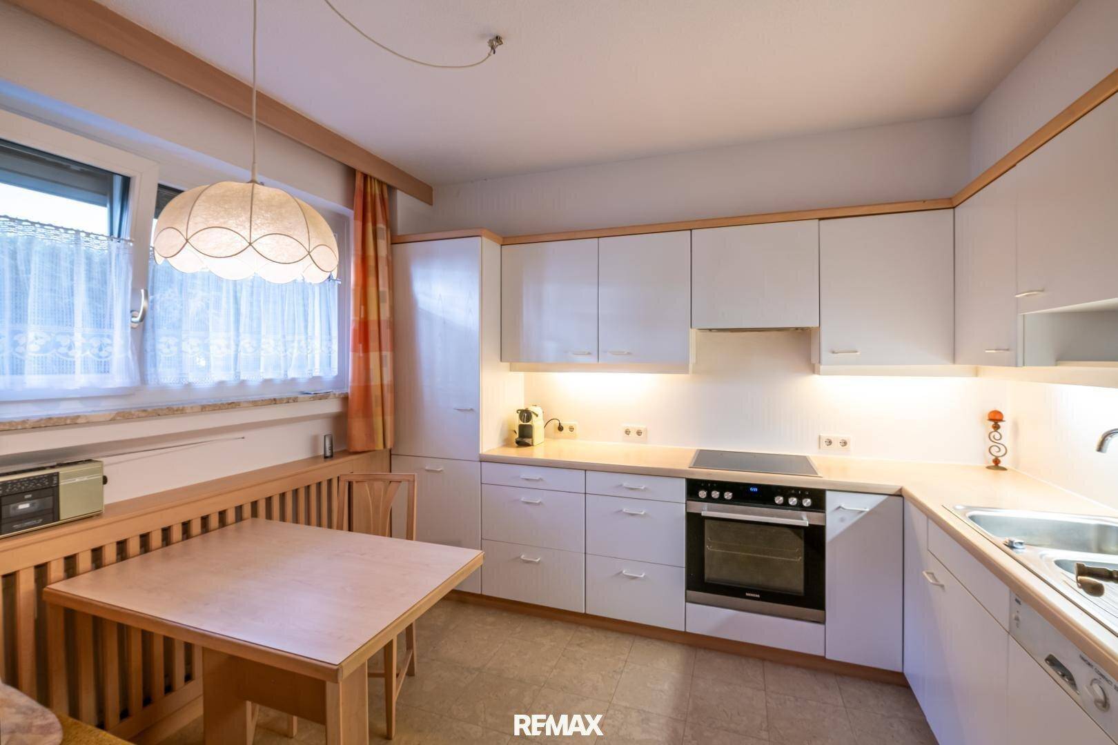 Funktionale Küche mit weißen Schränken, Essbereich und Fenster für Tageslicht.