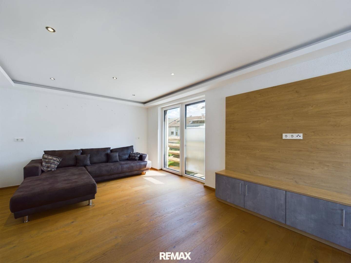 Geräumiges Wohnzimmer mit bequemer Couch, Holzboden und Zugang zum Außenbereich.