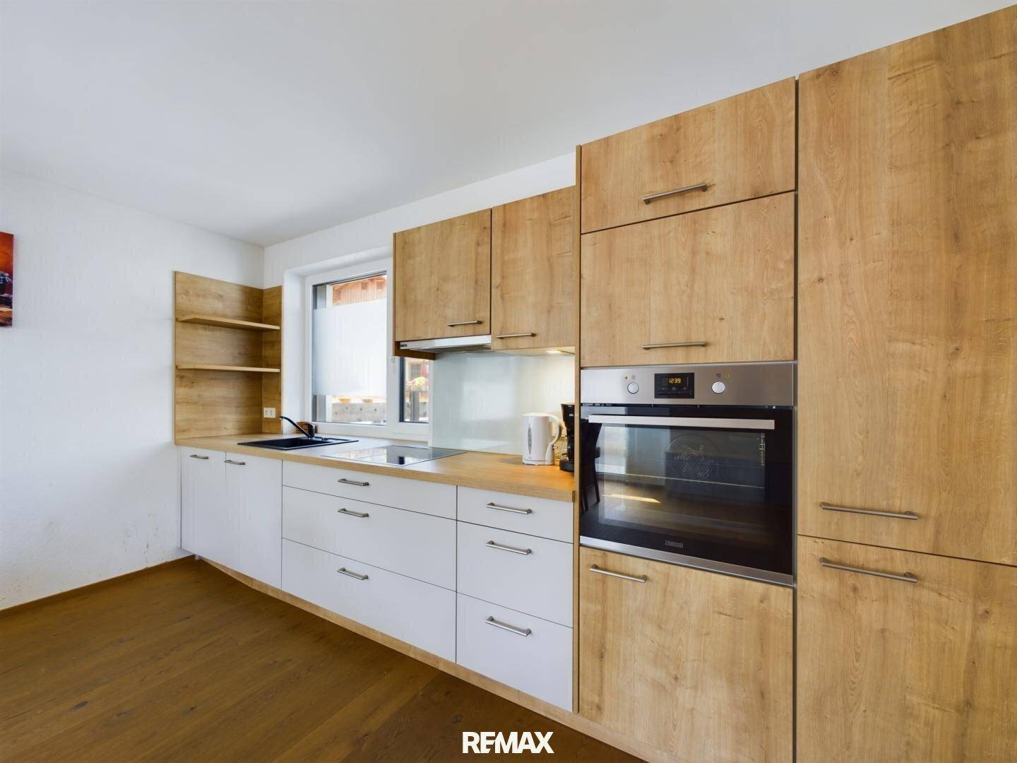 Funktionale Küche mit Holz- und weißen Fronten, integriertem Backofen und Fenster.