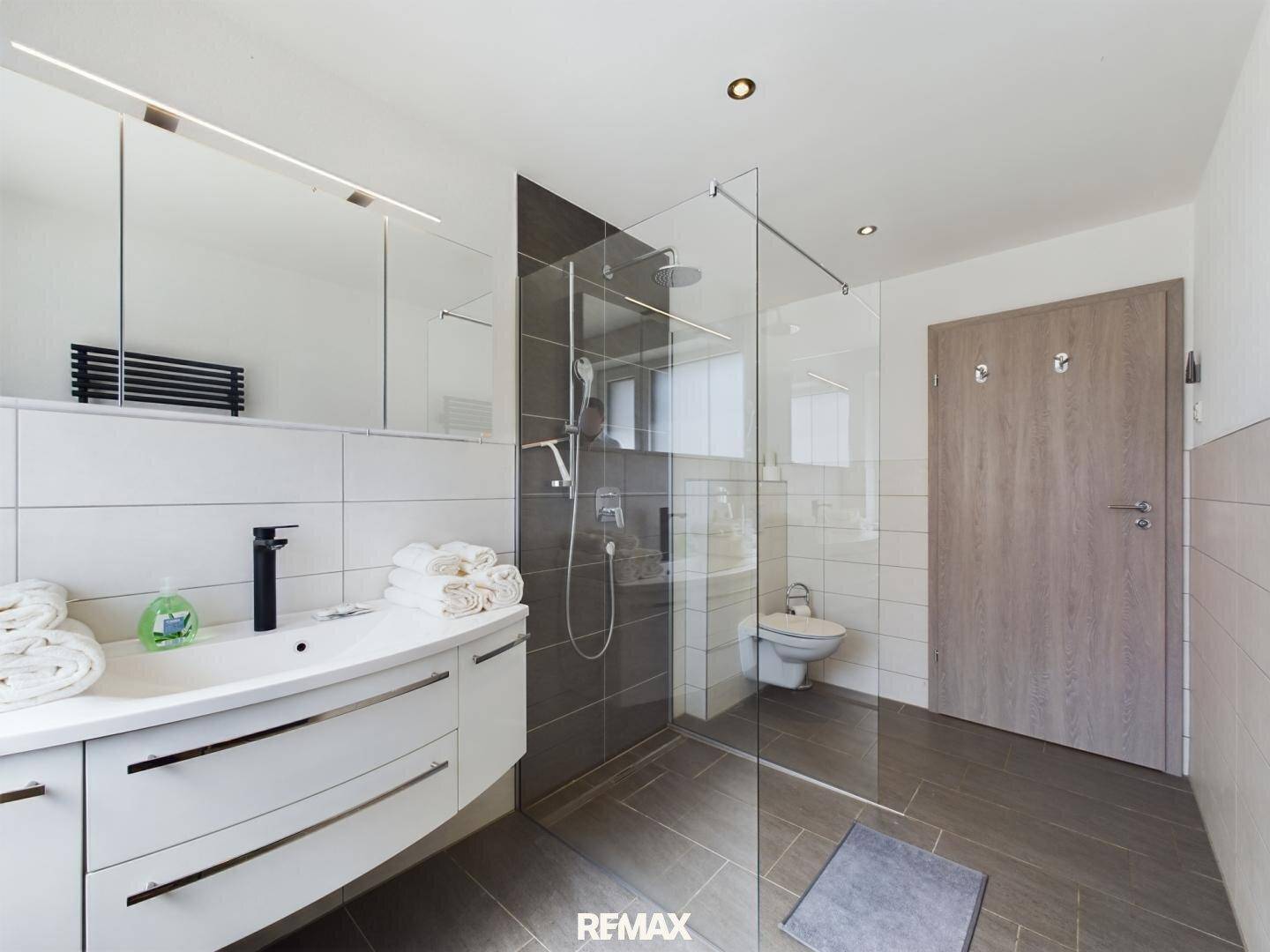 Modernes Badezimmer mit großer ebenerdiger Dusche, Waschtisch und WC.
