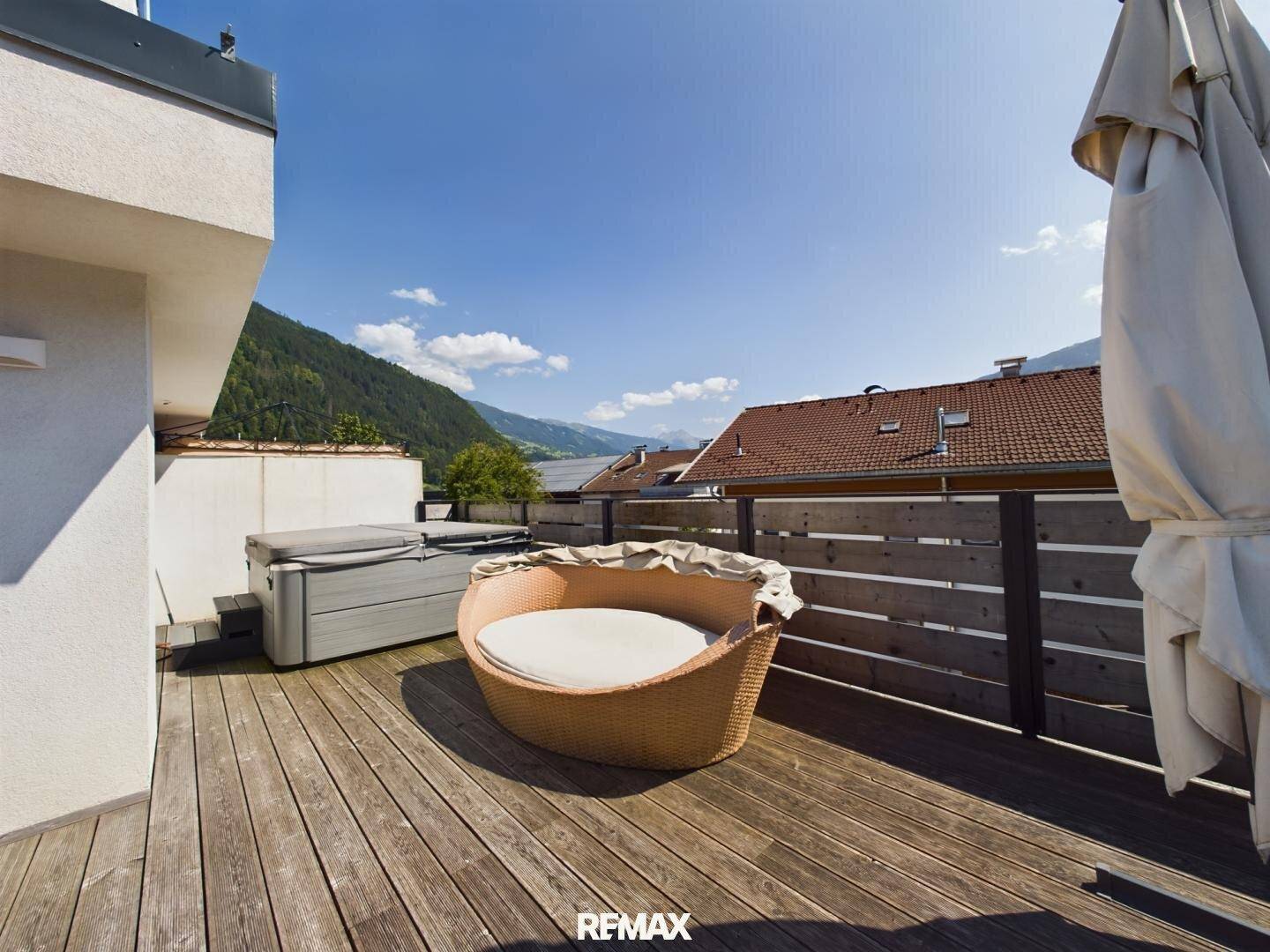 Sonnenterrasse mit Holzdeck, Whirlpool und Bergblick unter blauem Himmel.