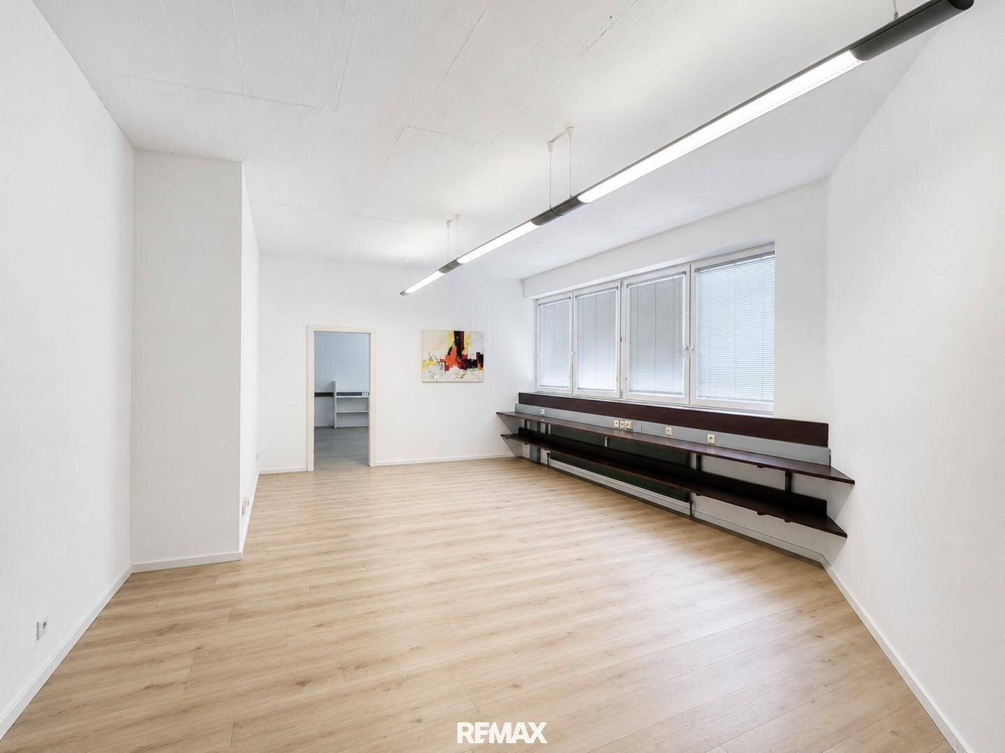 Heller Büroraum mit langen Fenstern, integrierten Regalen und einem modernen Kunstwerk an der Wand.