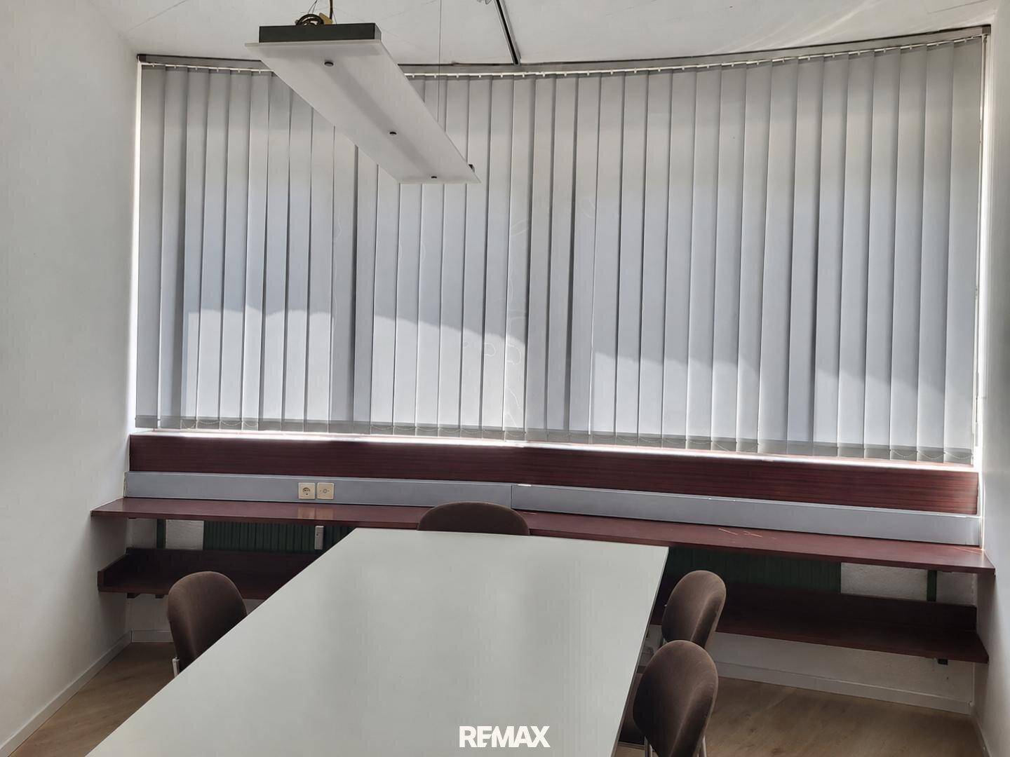 Besprechungsraum mit gebogener Fensterfront, vertikalen Jalousien und einem langen Konferenztisch.