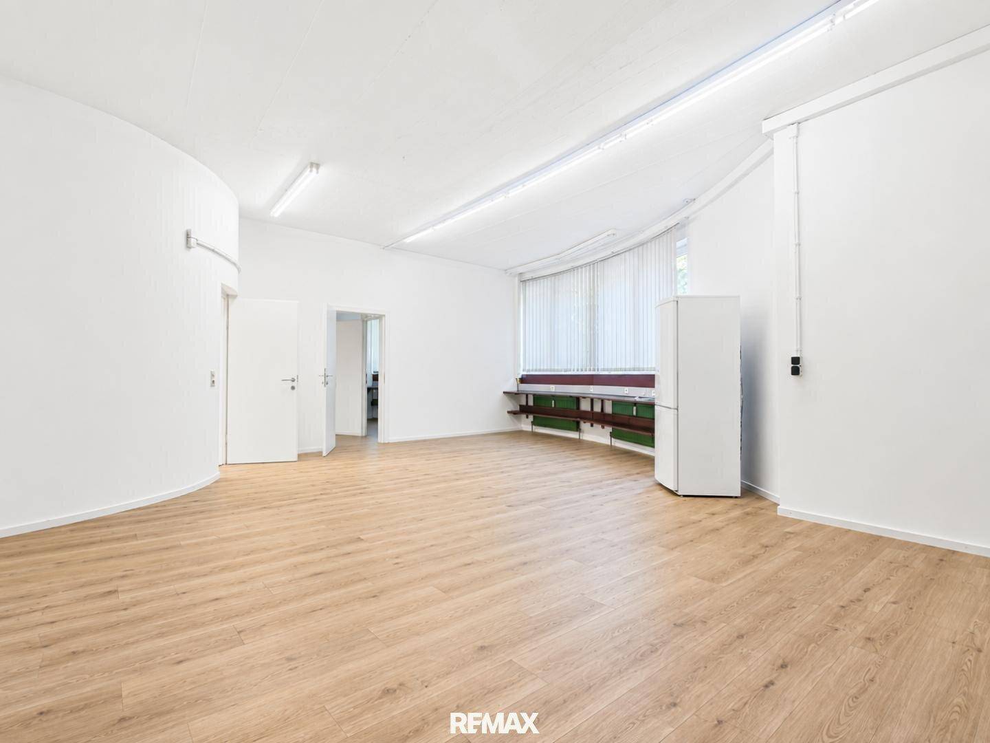 Geräumiger Bürobereich mit hellen Wänden, Laminatboden und einem Kühlschrank in der Ecke.