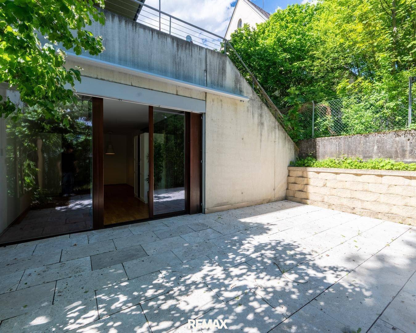 Helle Terrasse mit großen Glasfronten zum Innenbereich und umgeben von viel Grün.