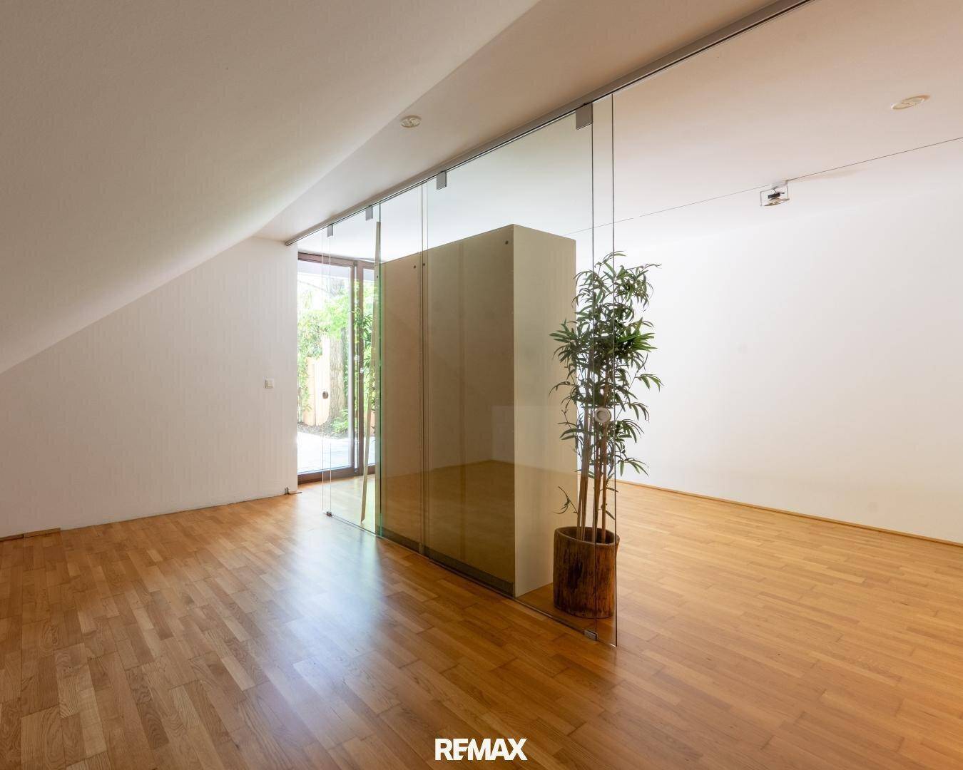Heller Wohnraum mit Dachschräge, Holzboden und großen Glasfronten, die viel Tageslicht hereinlassen.