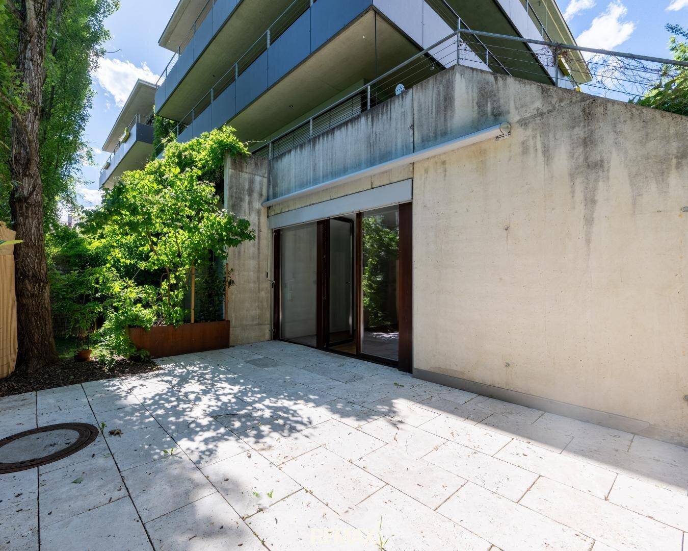 Geräumige Terrasse im Erdgeschoss mit Steinplatten und Zugang zu einem modernen Gebäude.