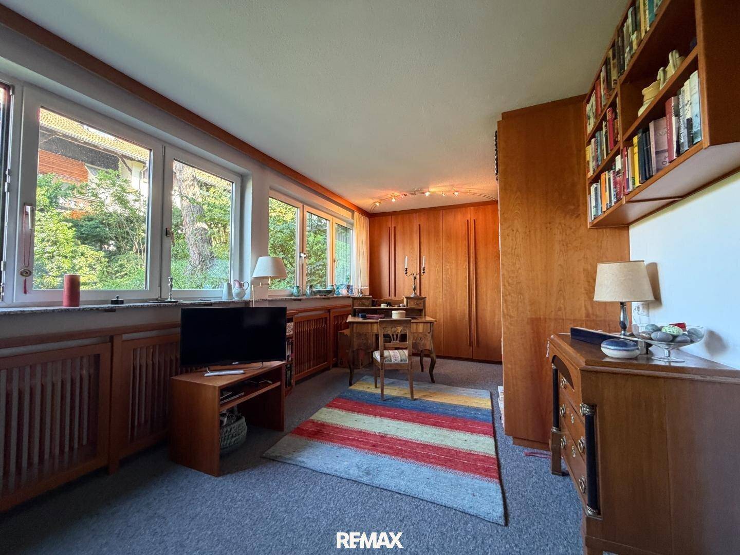 Funktionales Arbeitszimmer mit Holzvertäfelung, mehreren Fenstern und einem farbenfrohen Teppich.