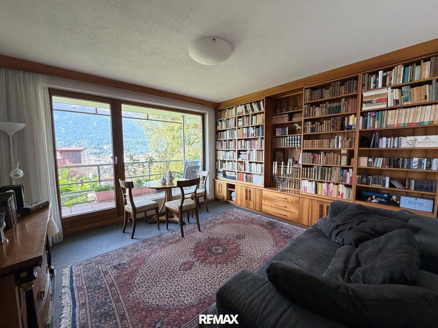 Helles Zimmer mit raumhohen Bücherregalen, gemütlichem Sofa und einem kleinen Essbereich mit Bergblick.