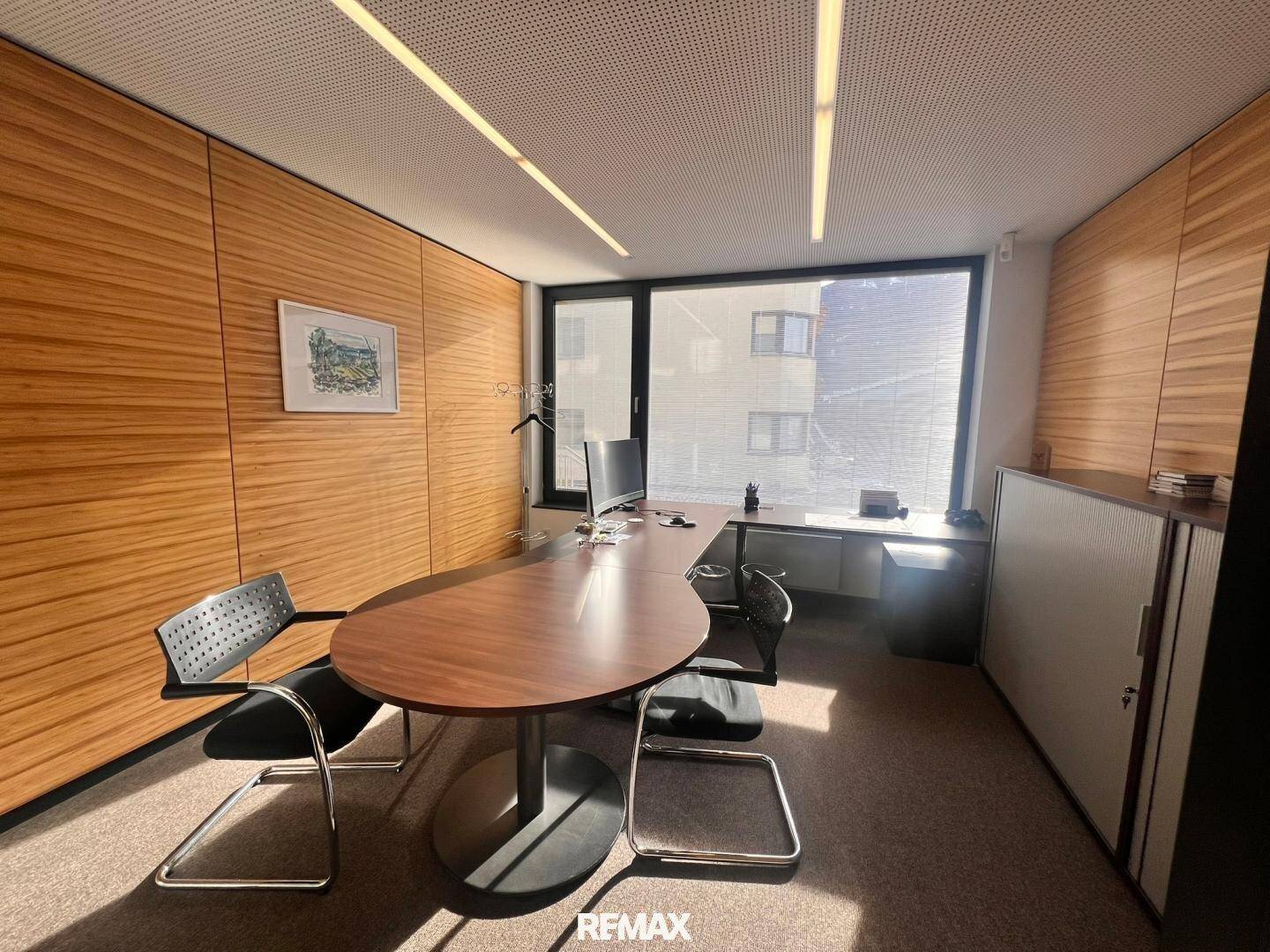 Helles Büro mit Holzwänden, einem großen ovalen Schreibtisch und bequemen Bürostühlen.
