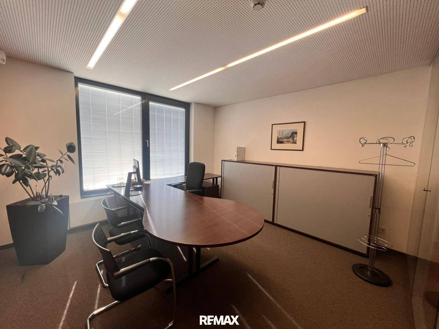 Funktionales Büro mit großem Schreibtisch, Bürostühlen und Schränken, gut beleuchtet.