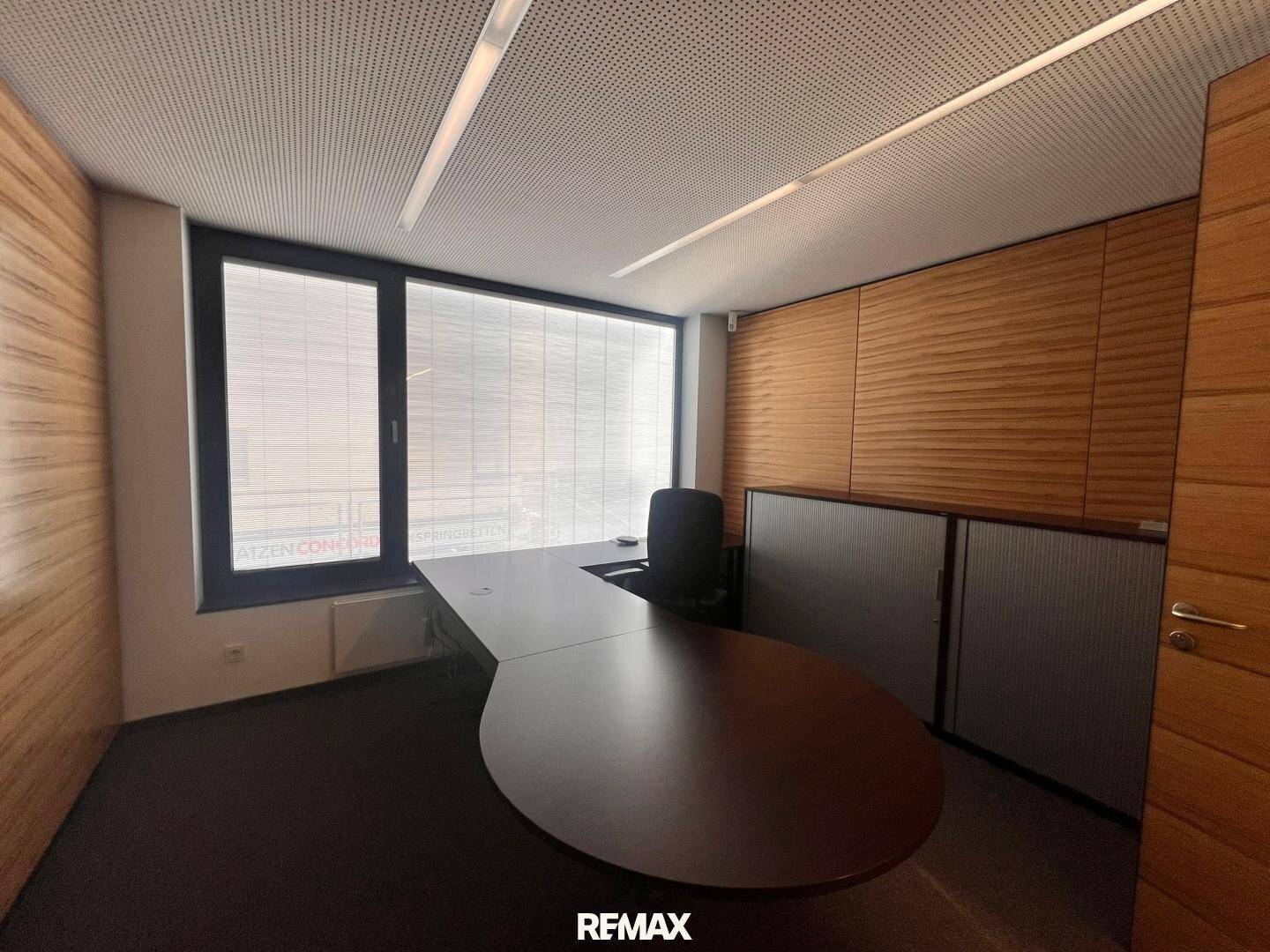 Modernes Büro mit Holzwänden, großem Schreibtisch und Blick nach draußen durch die Fenster.