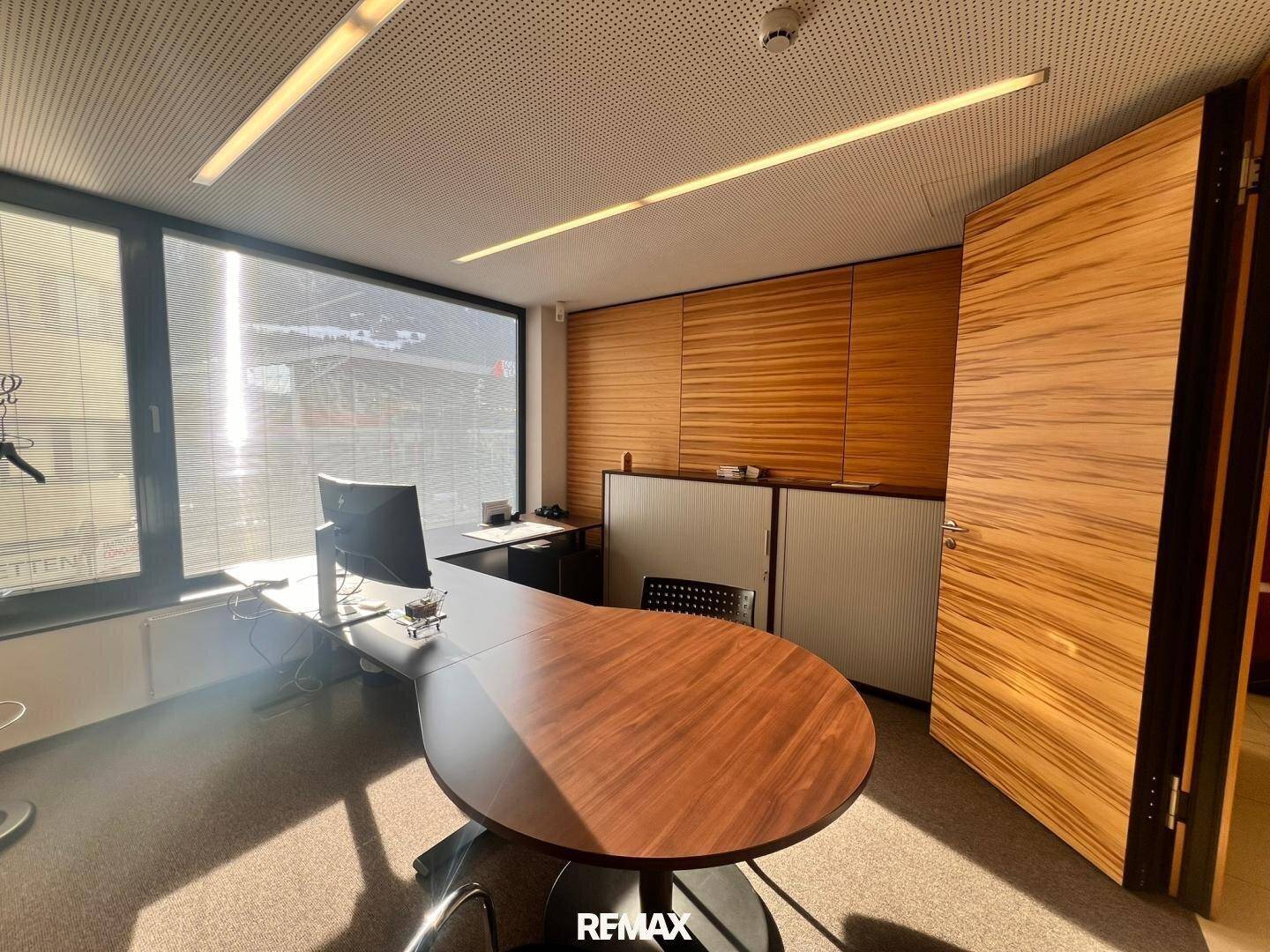 Geräumiges Büro mit Holzwänden, einem modernen Schreibtisch und viel Tageslicht durch die Fenster.