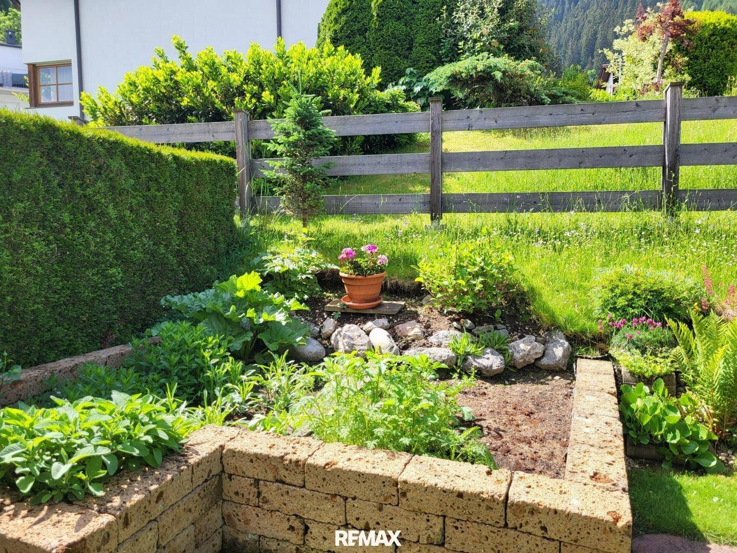 Kleiner Kräutergarten mit Steinumrandung und verschiedenen Pflanzen.