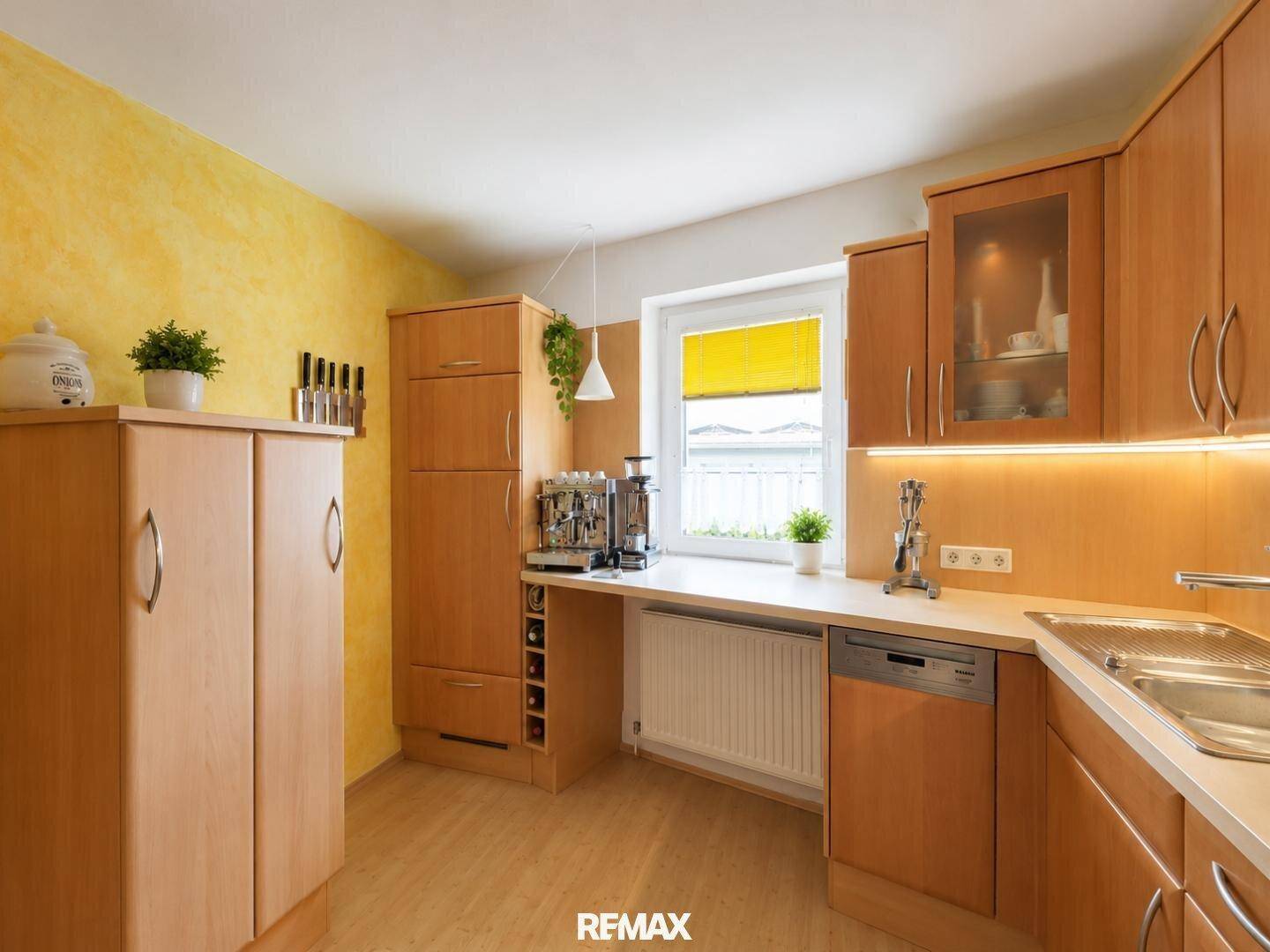 Funktionale Küche mit Holzschränken, gelber Wand und Fenster mit Blick ins Grüne.