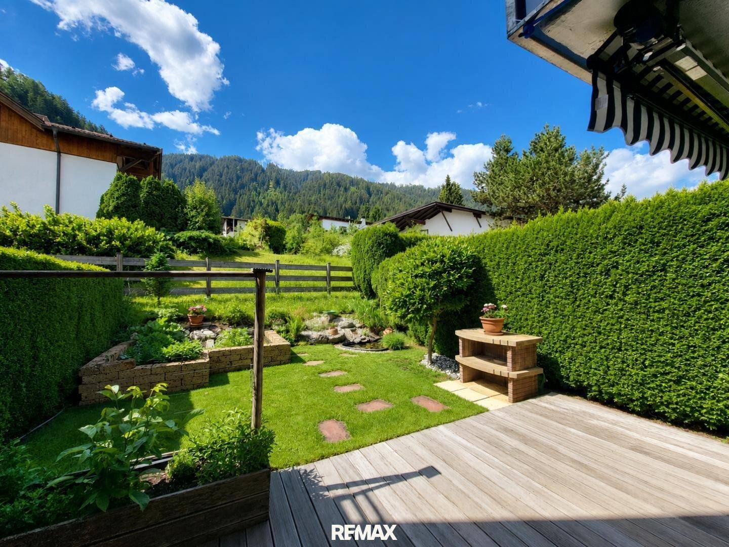 Gepflegter Garten mit Holzterrasse, Rasenfläche und üppiger Bepflanzung.