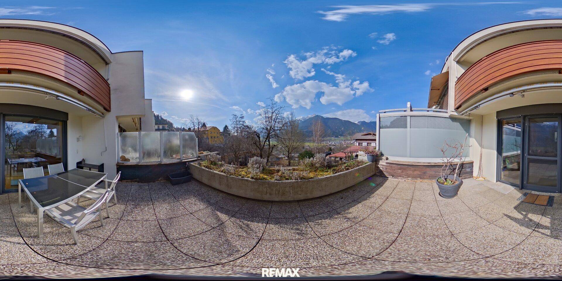 Panoramablick auf die sonnige Terrasse mit Sitzgelegenheiten und Bergblick.
