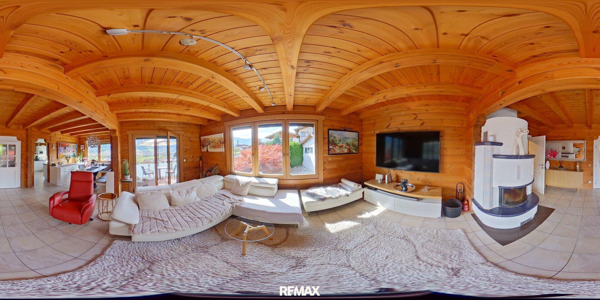 Gemütliches Wohnzimmer im Chalet-Stil mit Holzwänden, Kachelofen und großen Fenstern mit Aussicht.