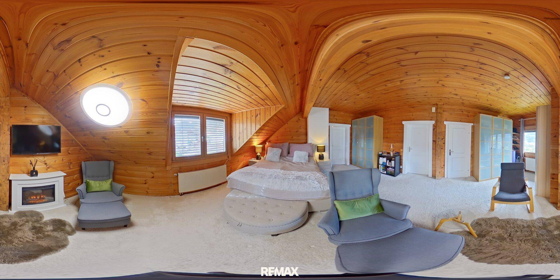 Geräumiges Schlafzimmer im Dachgeschoss mit Holzwänden, Teppichboden und gemütlicher Sitzecke.
