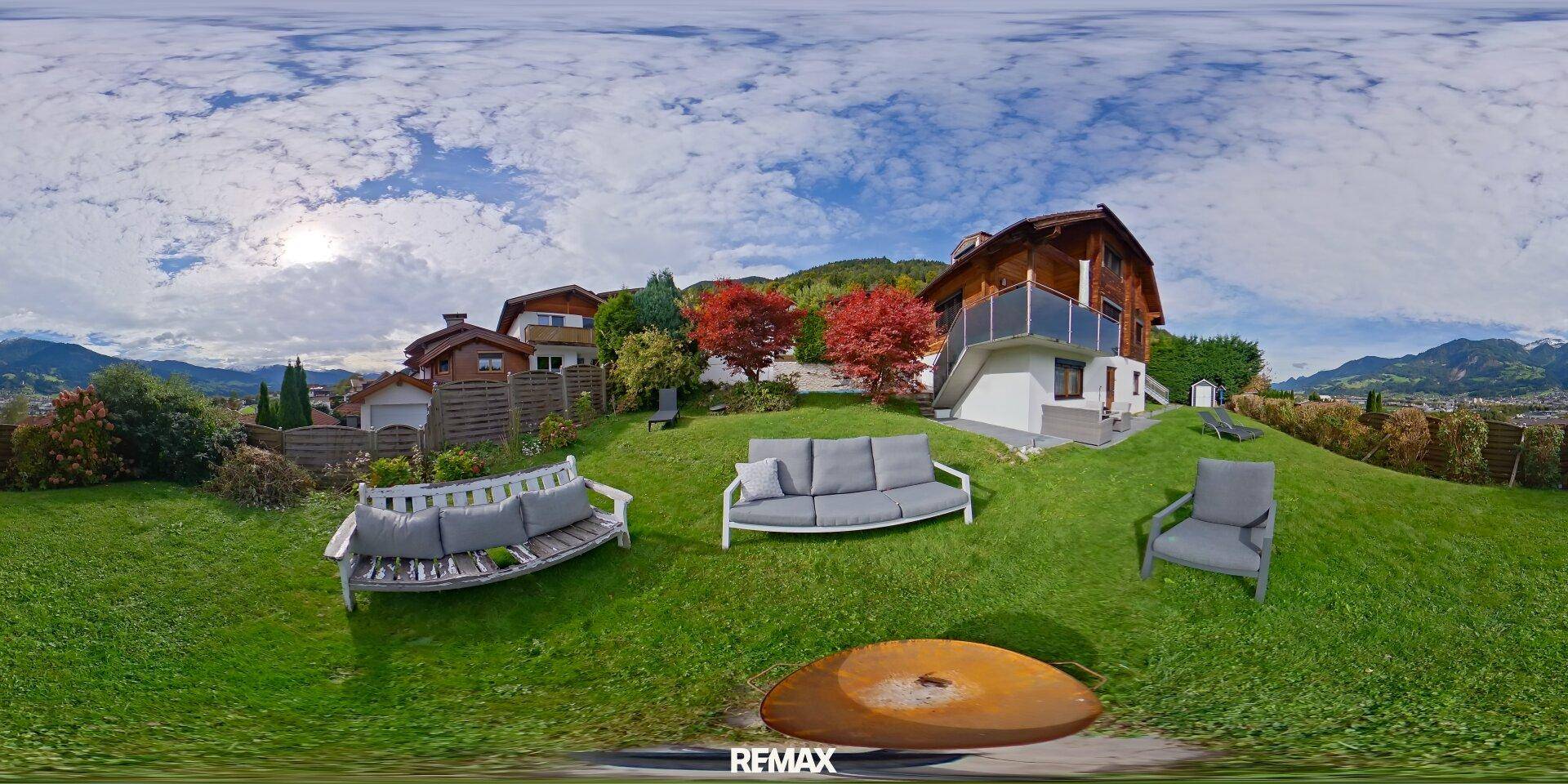 Großer, gepflegter Garten mit Sitzgelegenheiten und Blick auf das Holzhaus und die Berge.