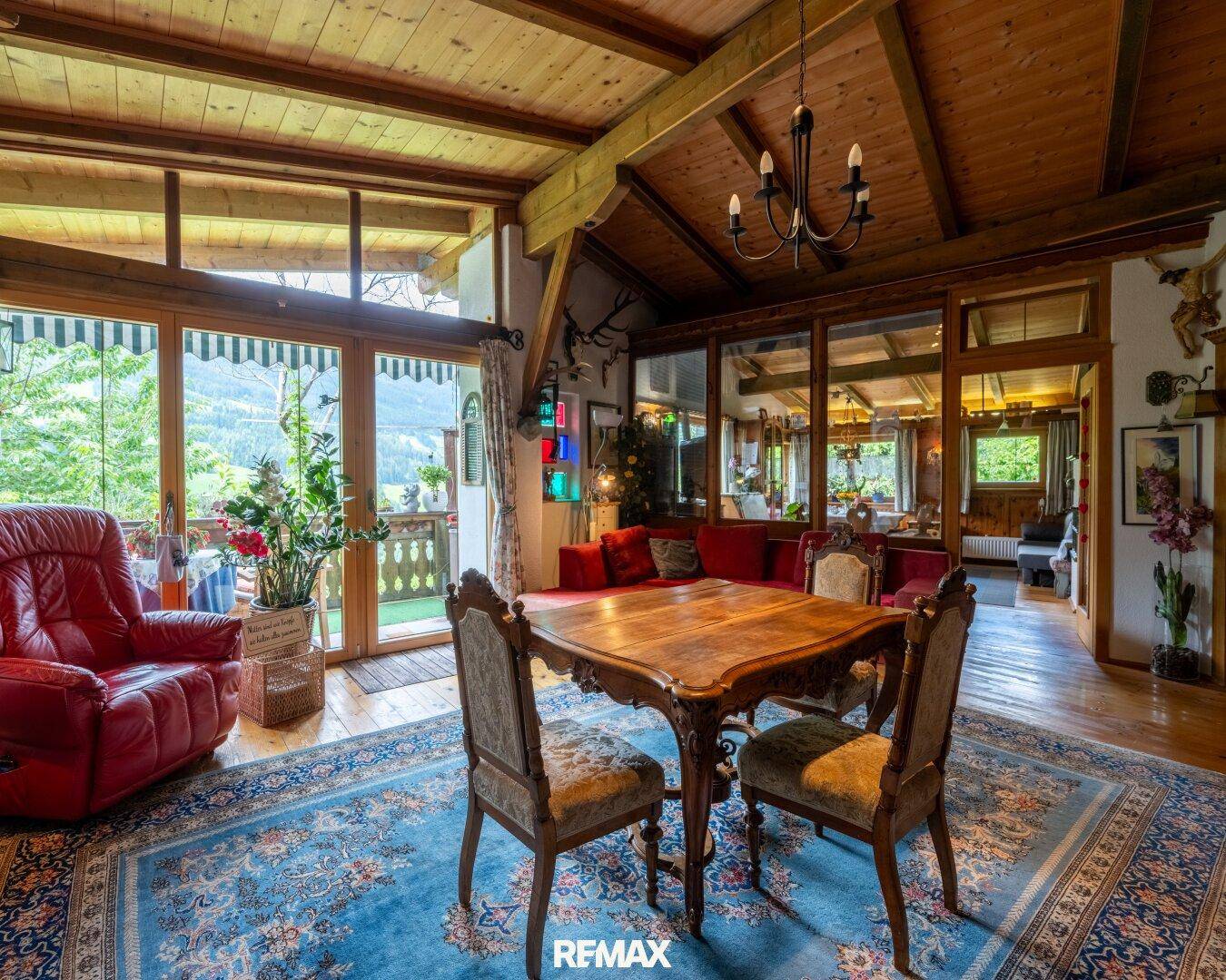 Traditionelles Wohnzimmer mit Holzbalkendecke, gemütlichen Möbeln und Zugang zu einem Balkon mit Bergblick.