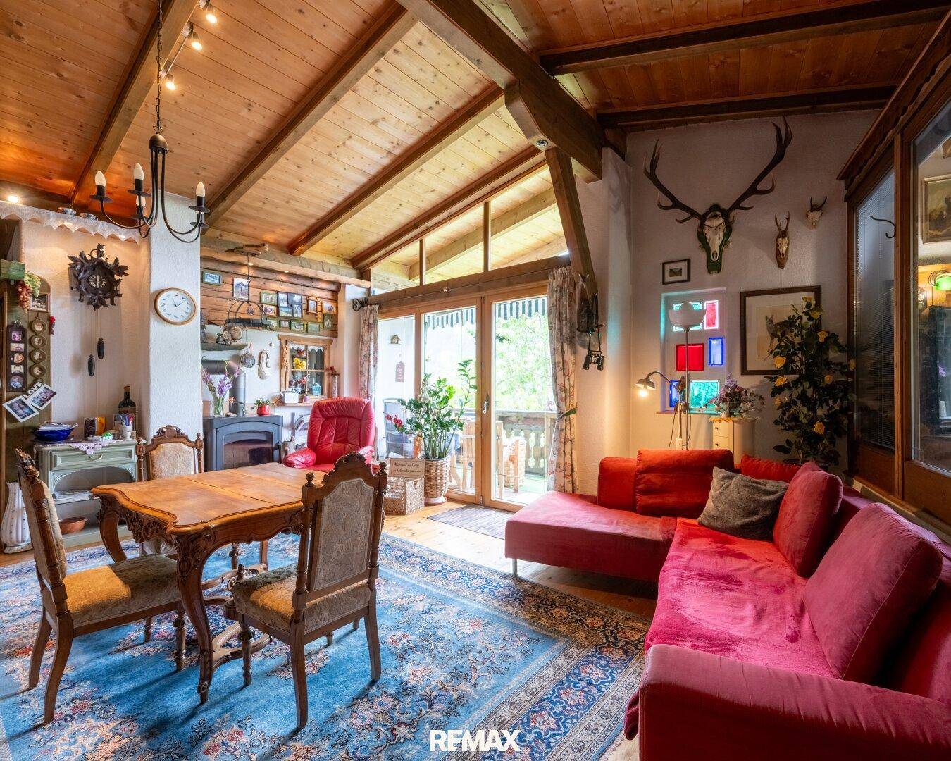 Rustikales Wohnzimmer mit rotem Sofa, Holzbalken und traditioneller Dekoration, mit Zugang zum Außenbereich.
