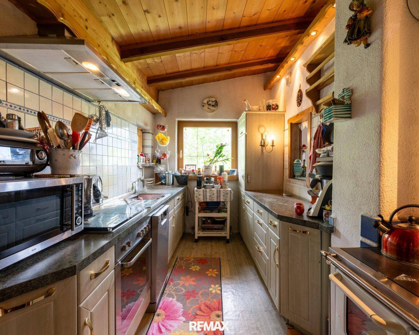 Funktionale Küche im Landhausstil mit Holzbalkendecke, Fliesen und Blick ins Grüne.