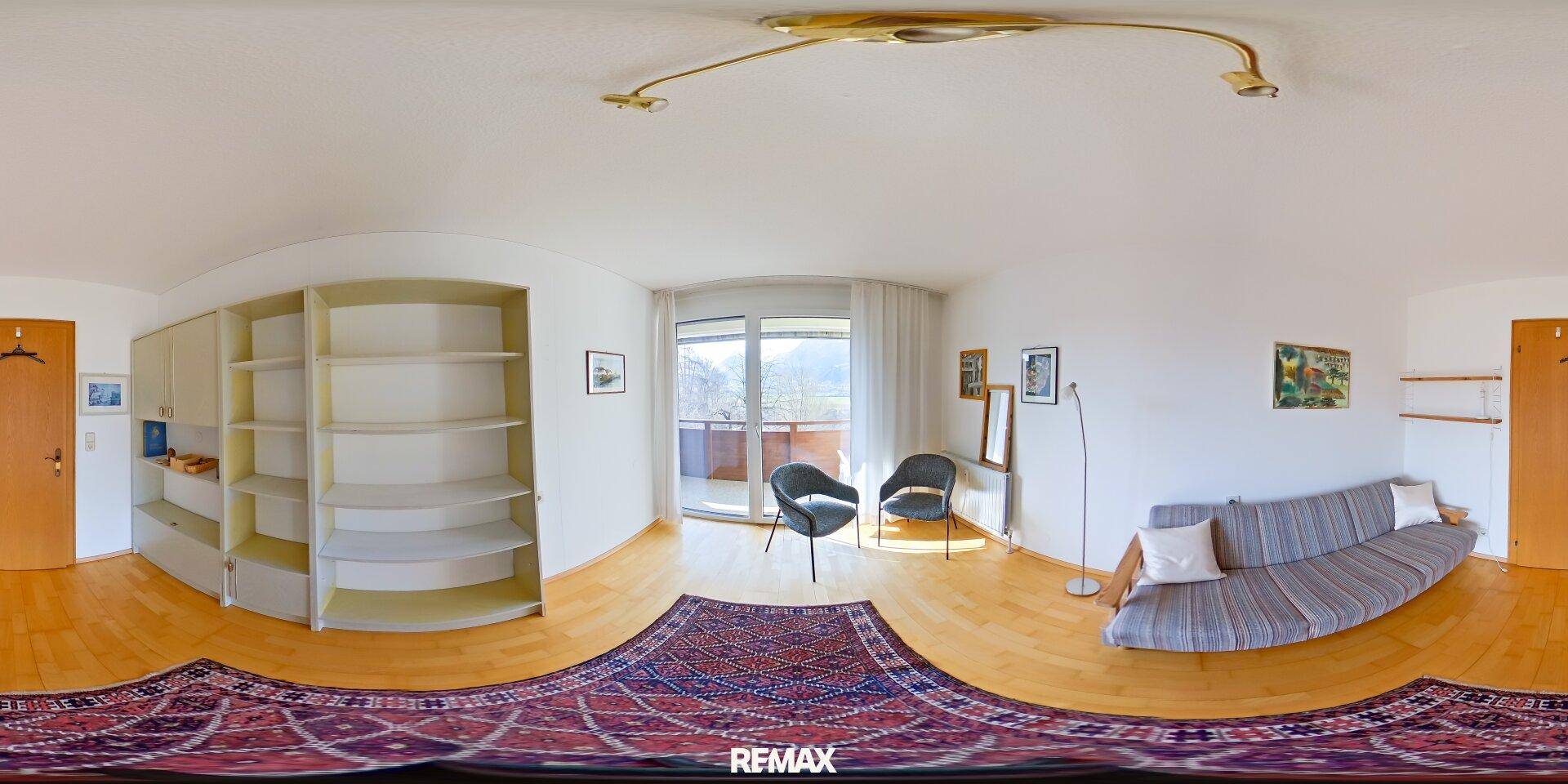 Helles Wohnzimmer mit Holzboden, Regalen und Zugang zu einem Balkon mit Bergblick.