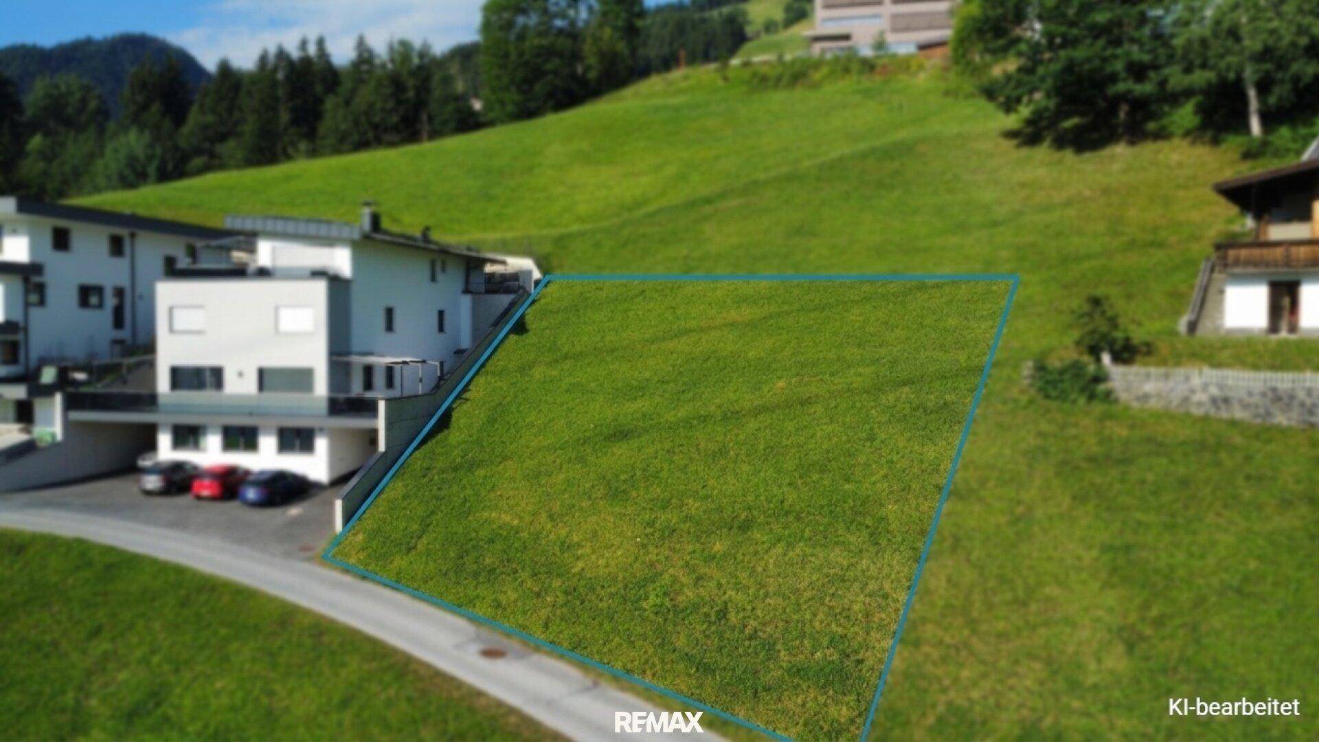 Luftaufnahme eines grünen Baugrundstücks am Hang, umgeben von moderner Architektur und Natur.