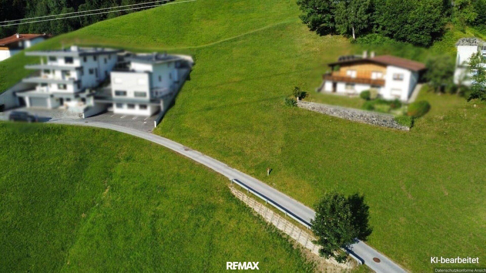 Panoramablick auf eine grüne Hanglandschaft mit einer Straße und verschiedenen Gebäuden in der Ferne.