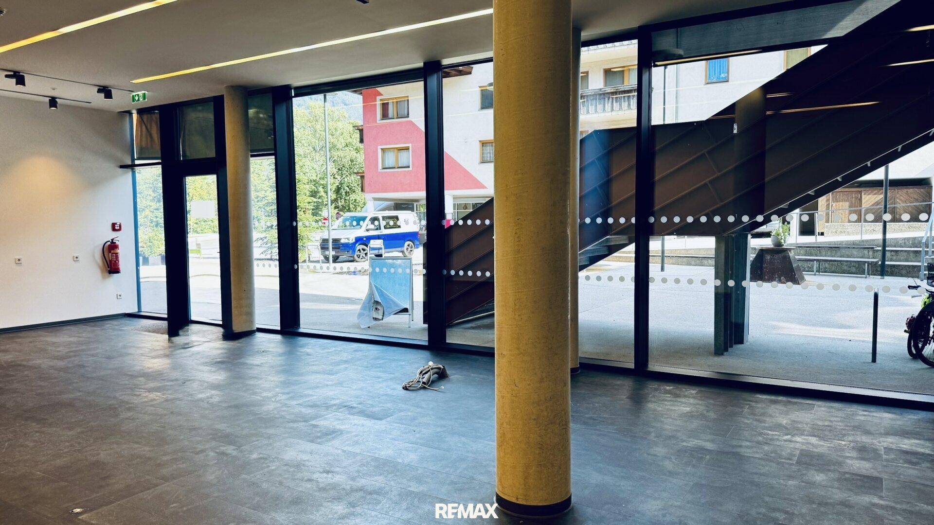 Heller Gewerberaum mit großen Glasfronten, die den Blick auf die Straße und die Außentreppe freigeben.