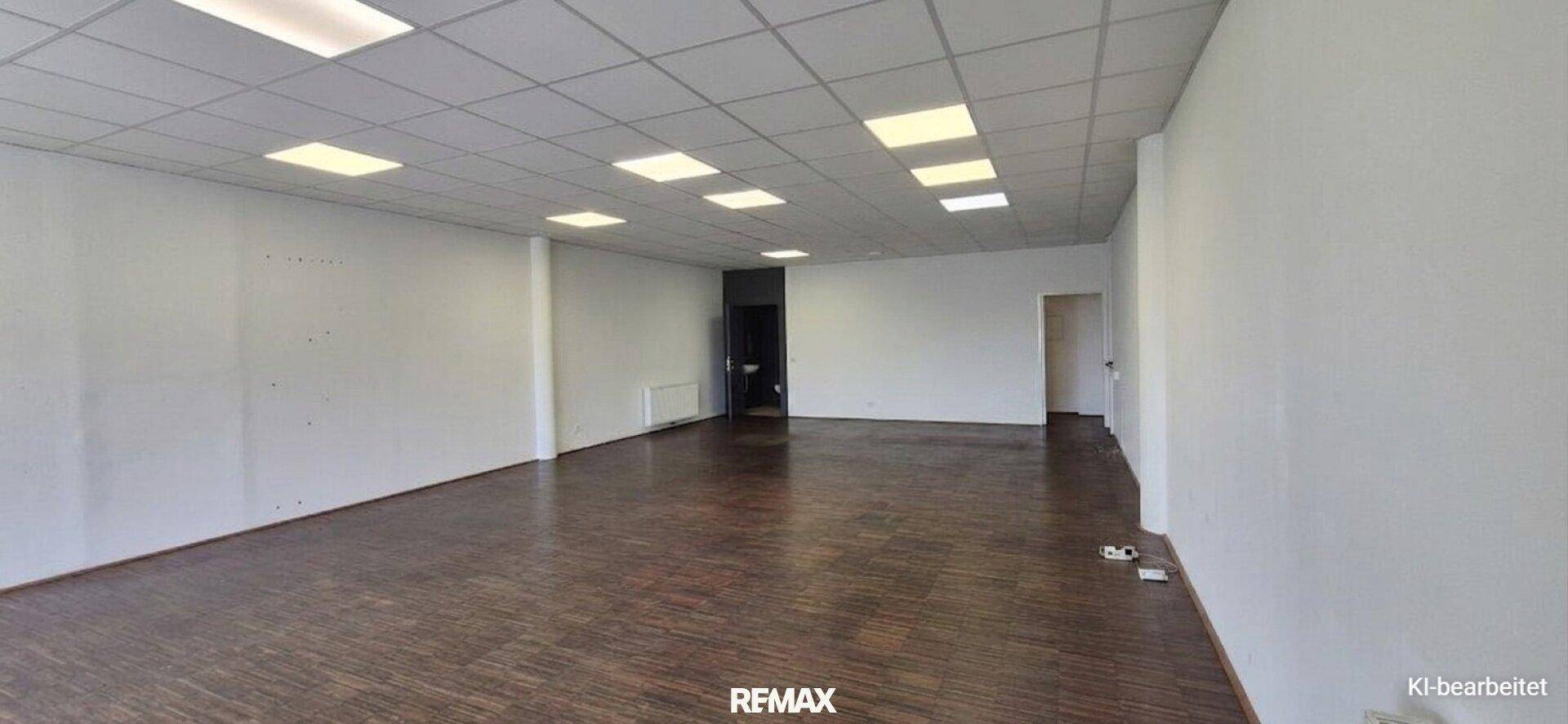 Weiterer Blick in den geräumigen Gewerberaum mit dunklem Boden und Zugang zu Nebenräumen.