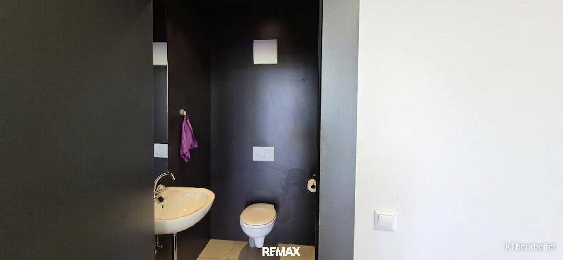 Kleines WC mit dunklen Wänden, weißer Toilette und einem Waschbecken.