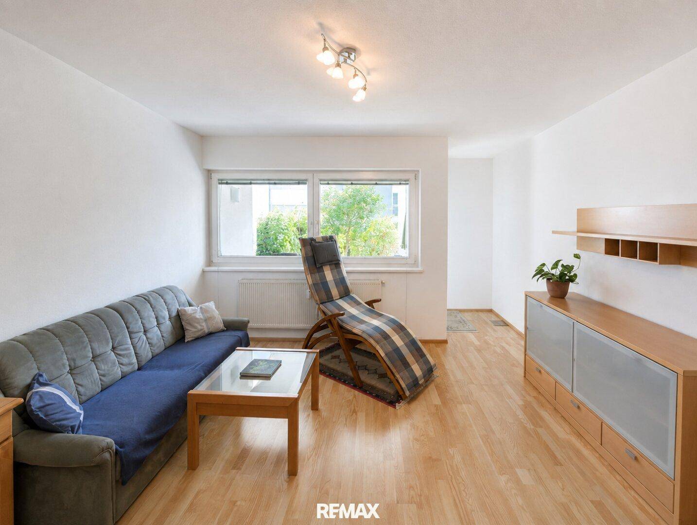 Helles Wohnzimmer mit Holzfußboden, bequemer Couch und einem Fenster mit Blick ins Grüne.