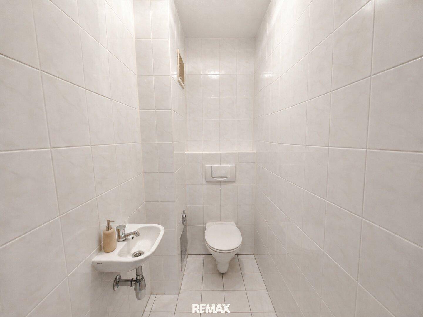 Gefliestes Gäste-WC mit wandhängender Toilette und kleinem Handwaschbecken, sehr gepflegt.