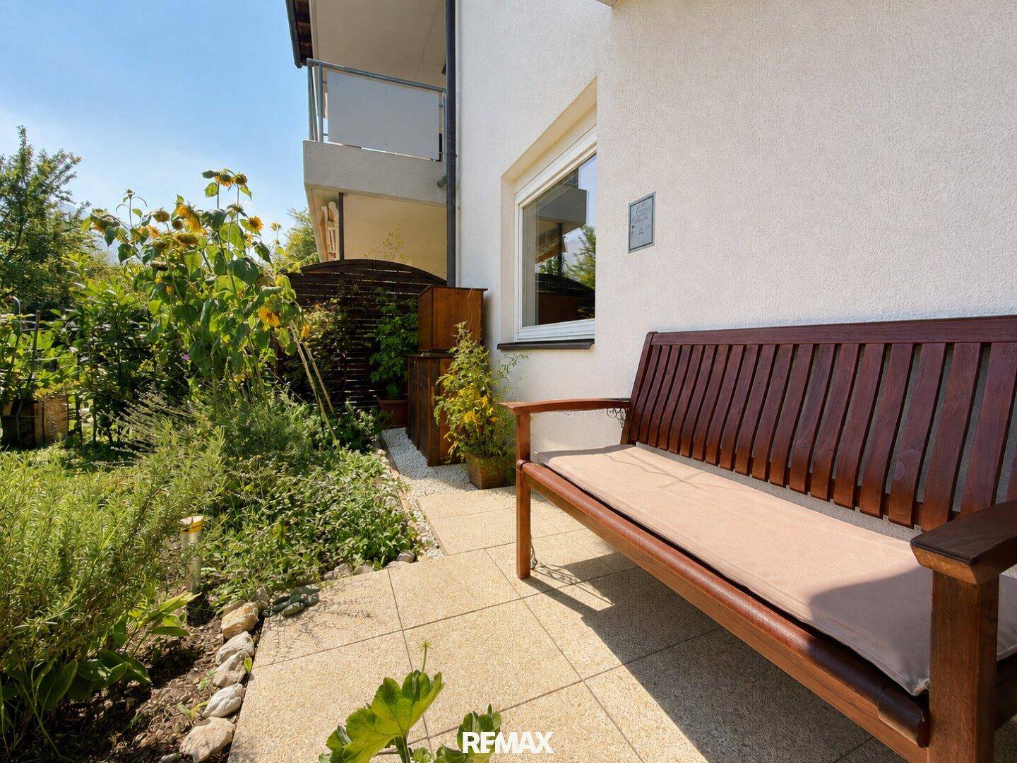 Gemütliche Terrasse mit Holzbank und üppiger Bepflanzung, ideal für entspannte Stunden im Freien.