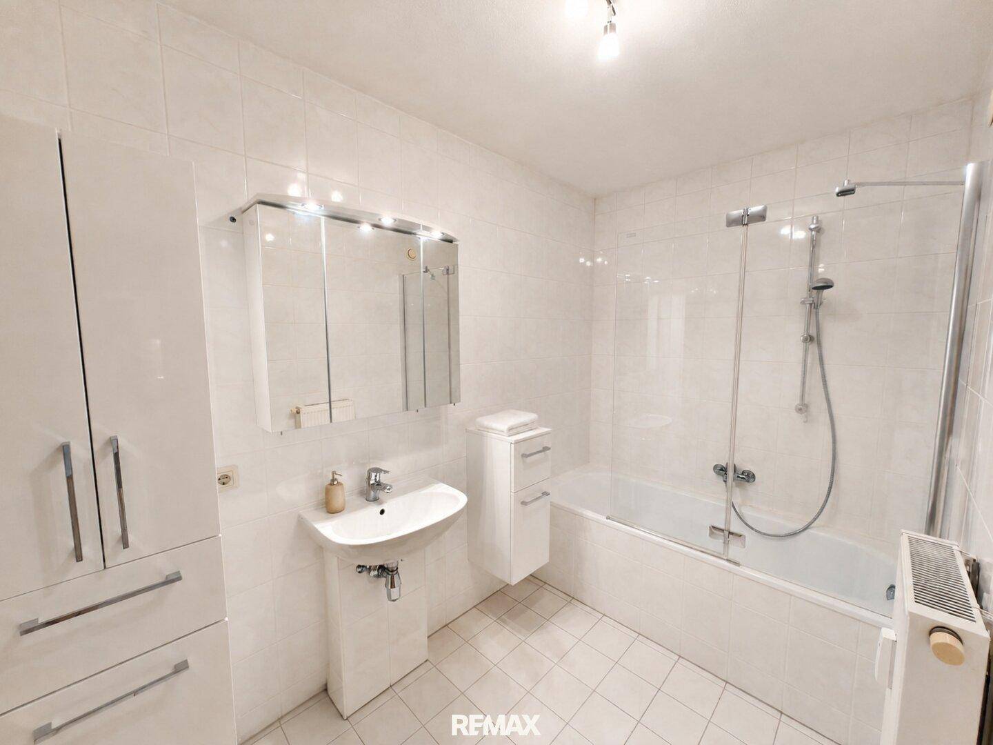 Modern gefliestes Badezimmer mit Badewanne, Duschabtrennung, Waschbecken und praktischen Schränken.
