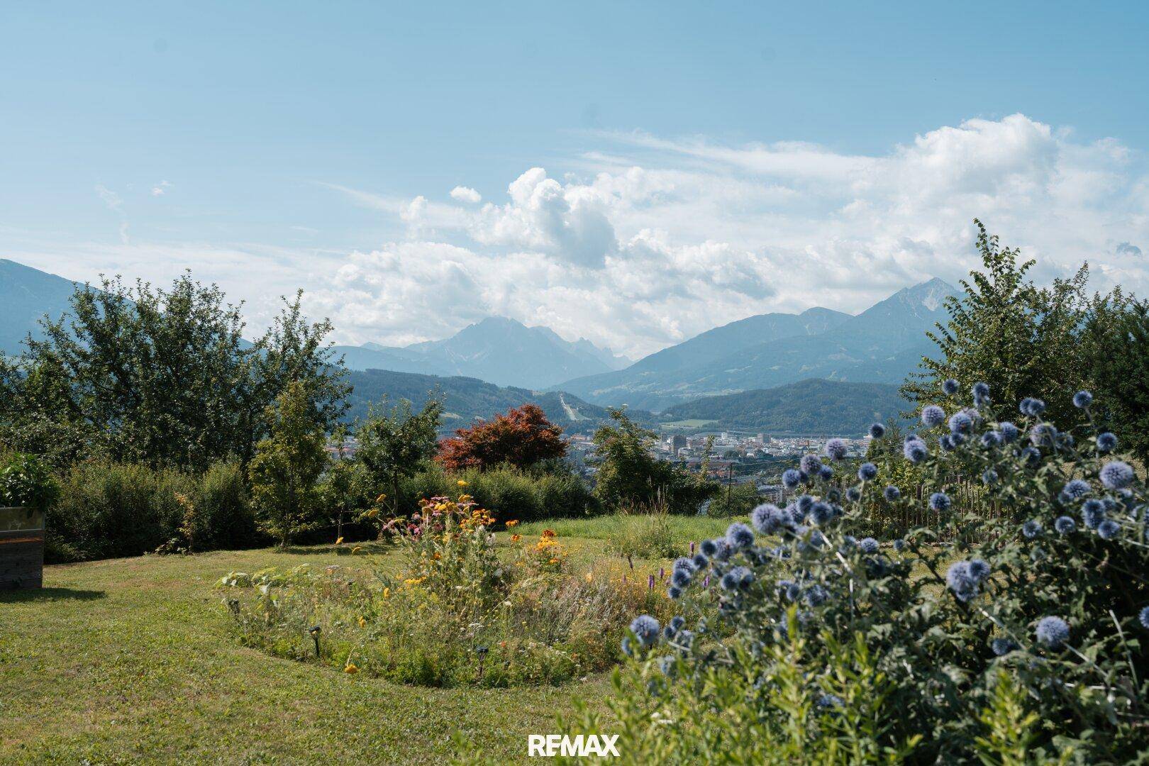 Weitläufiger Gartenbereich mit blühenden Pflanzen und einem malerischen Blick auf die Stadt und die umliegenden Berge.
