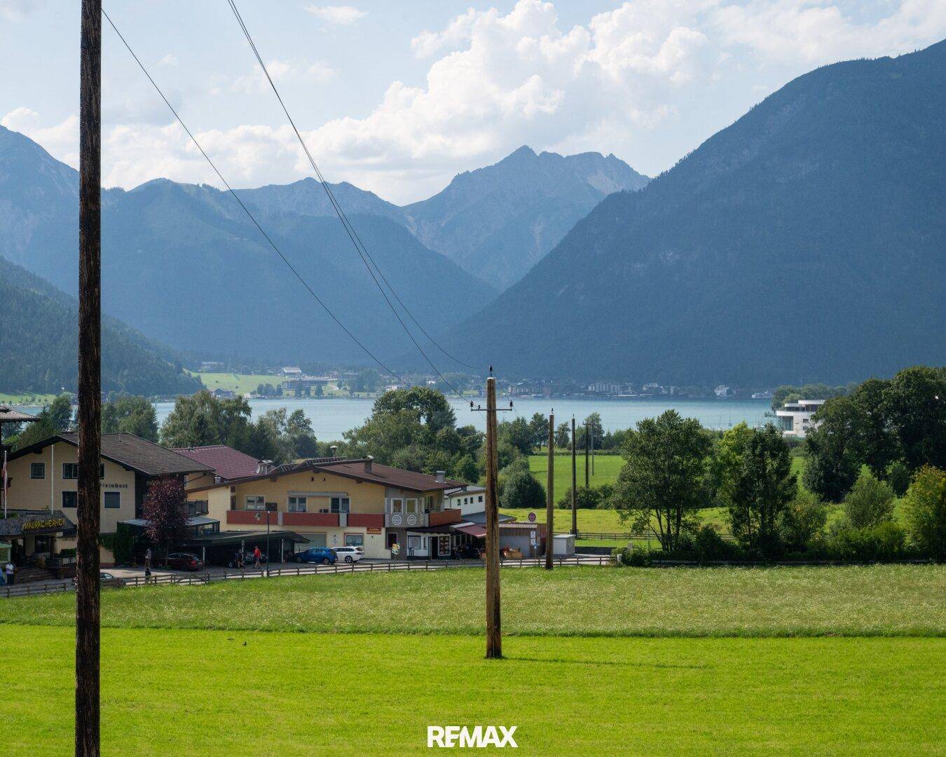 Weitläufiger Blick über grüne Felder auf einen See und die umliegenden Berge.