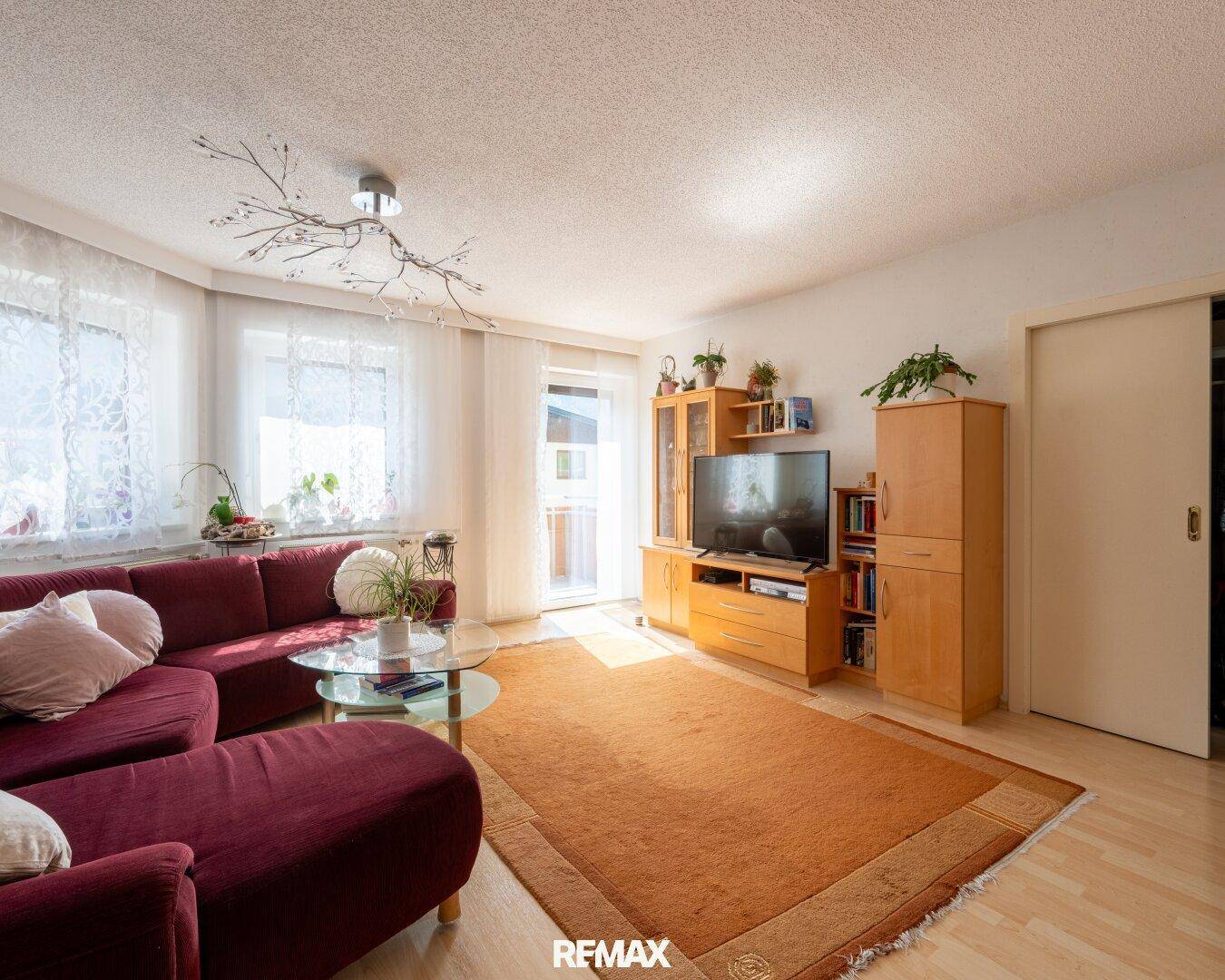 Helles Wohnzimmer mit großem Sofa, TV-Möbeln und Zugang zu einem Balkon.