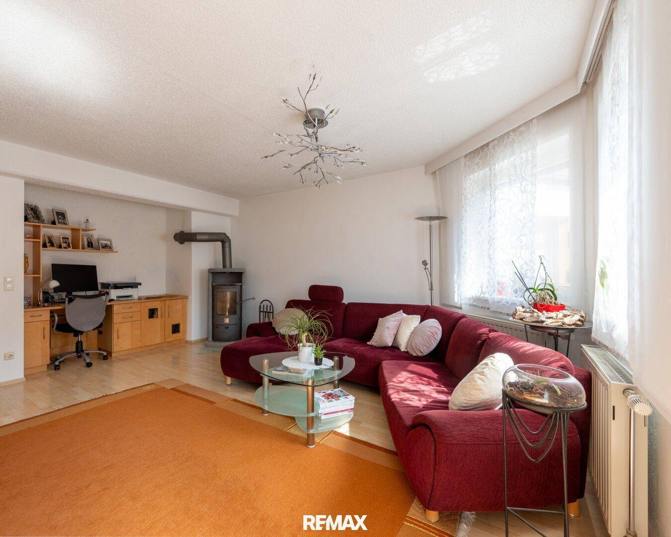 Gemütliches Wohnzimmer mit Kaminofen, rotem Sofa und hellem Parkettboden.