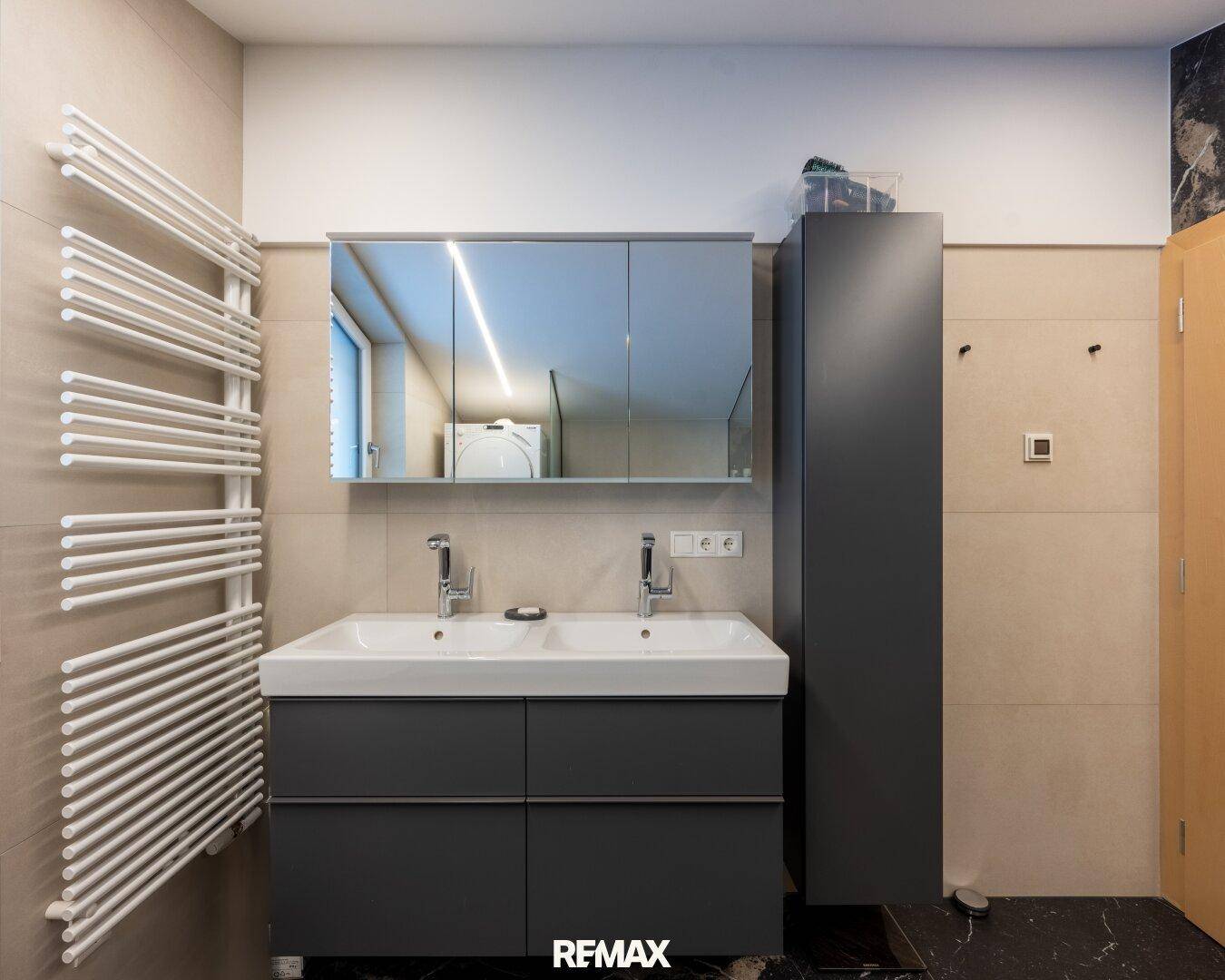 Modernes Badezimmer mit Doppelwaschbecken, Spiegelschrank und Handtuchheizkörper.