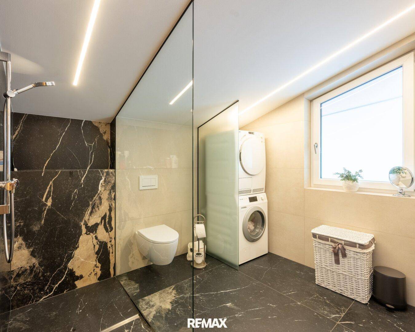 Elegantes Badezimmer mit begehbarer Dusche, WC und Waschmaschine im Dachgeschoss.
