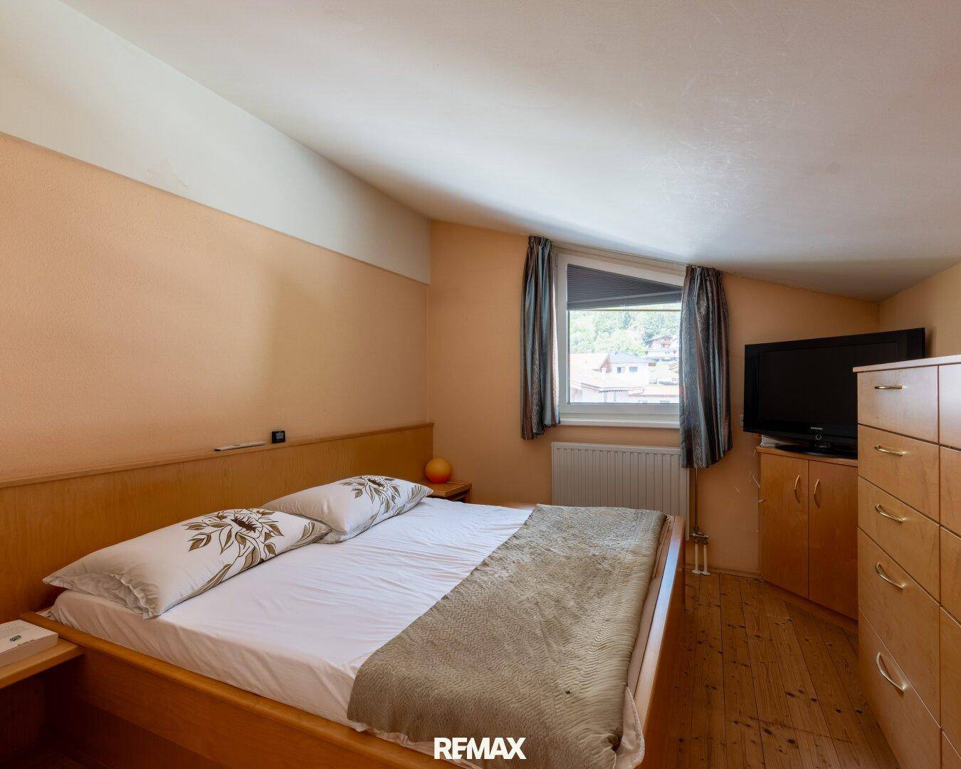 Schlafzimmer mit Holzbett, Dachschräge und Fenster mit Blick ins Grüne.