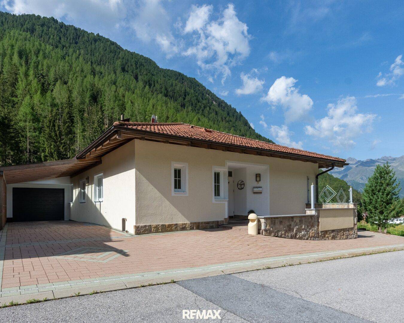 Charmantes Einfamilienhaus mit Carport und gepflasterter Auffahrt vor einer malerischen Bergkulisse.
