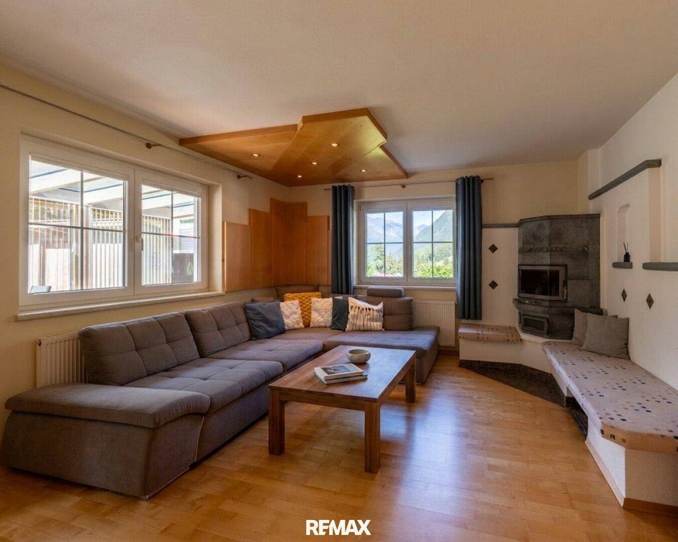 Gemütliches Wohnzimmer mit großem Sofa, Holzboden und traditionellem Kachelofen für warme Abende.
