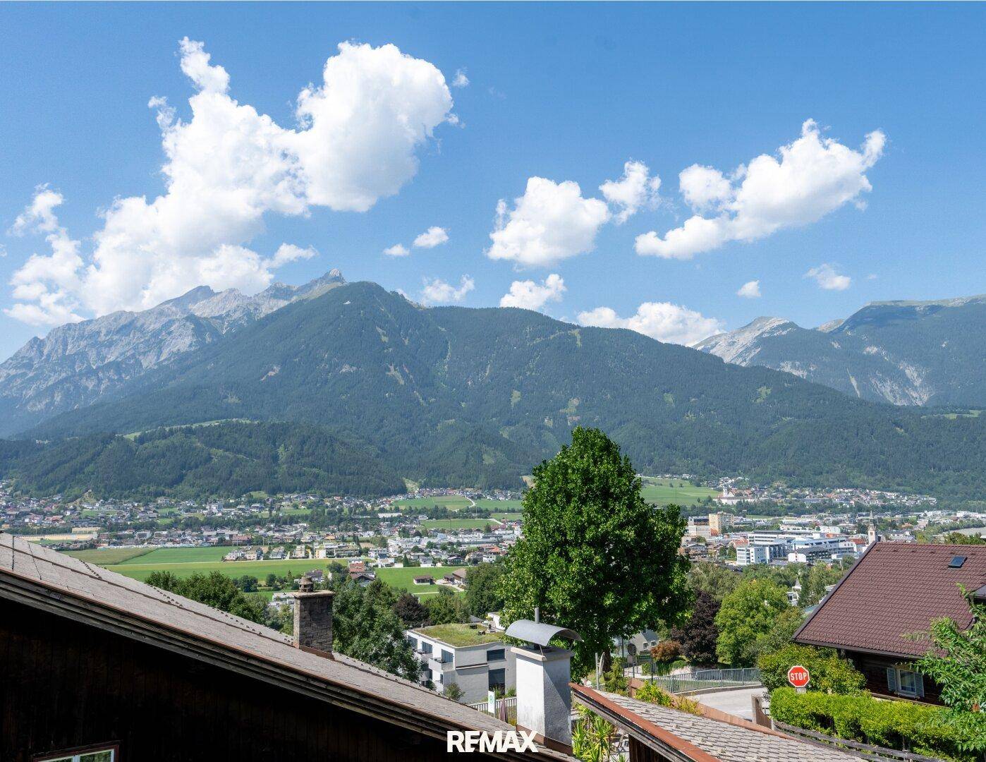 Panoramablick auf die umliegende Berglandschaft und das Tal mit Siedlungen unter blauem Himmel.