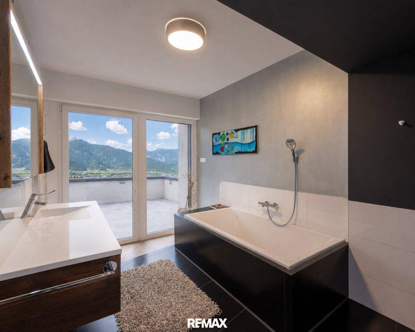 Modernes Badezimmer mit Badewanne, Doppelwaschbecken und Zugang zu einer Terrasse mit Bergblick.
